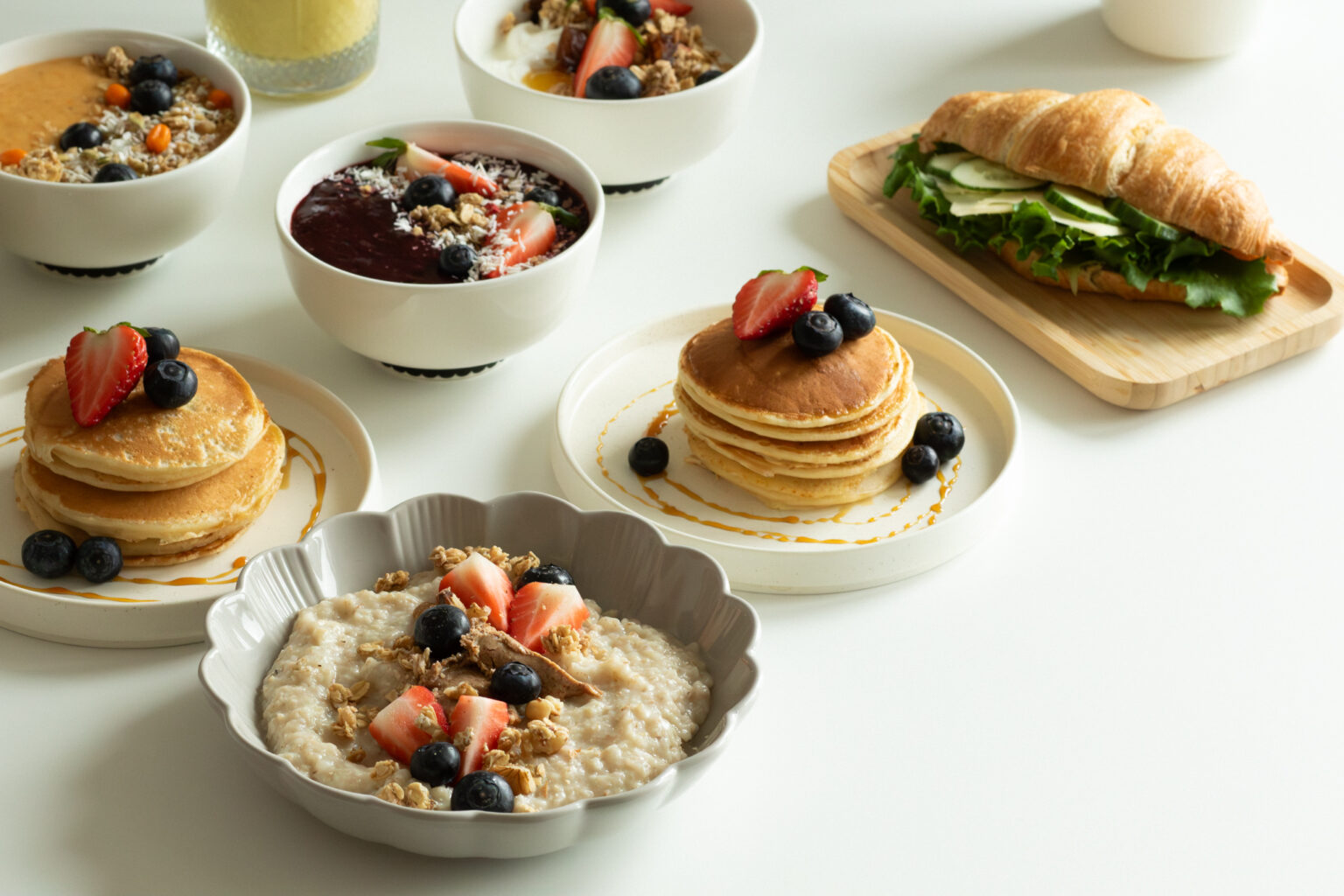 Pöydällä puuroa, minipannukakkuja, smoothie bowl ja täytetty sämpylä