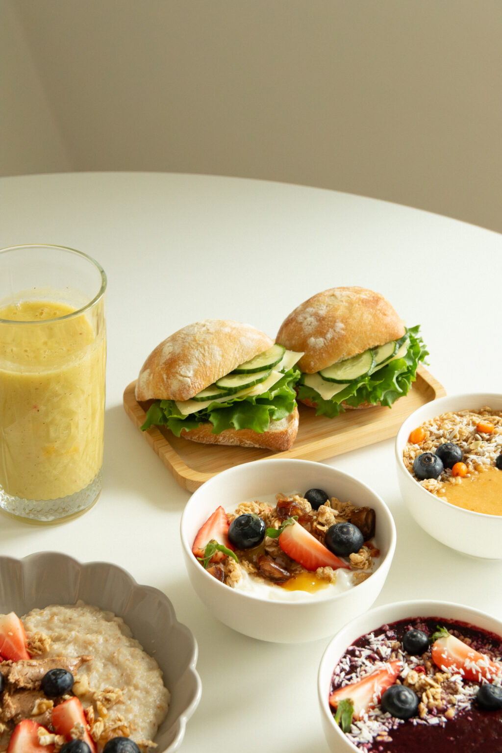 Pöydällä täytettyjä sämpylöitä, smoothieta ja aamiaiskulhoja